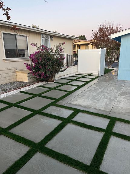 Residential front walkway with square stone pavers, grass, a flowering bush, and houses on both sides
