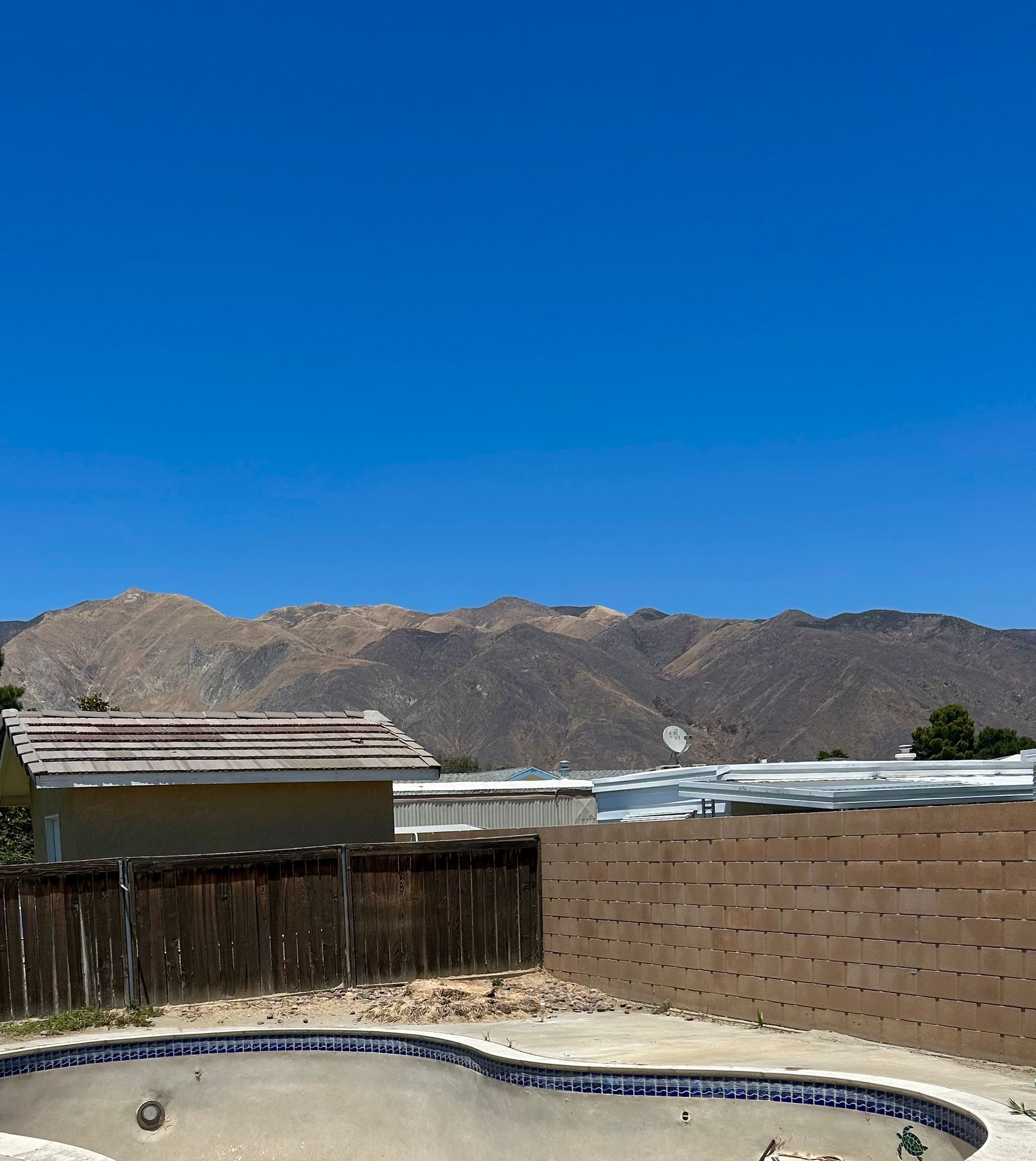 A swimming pool with mountains in the background and a house in the background. Palm tree removed.