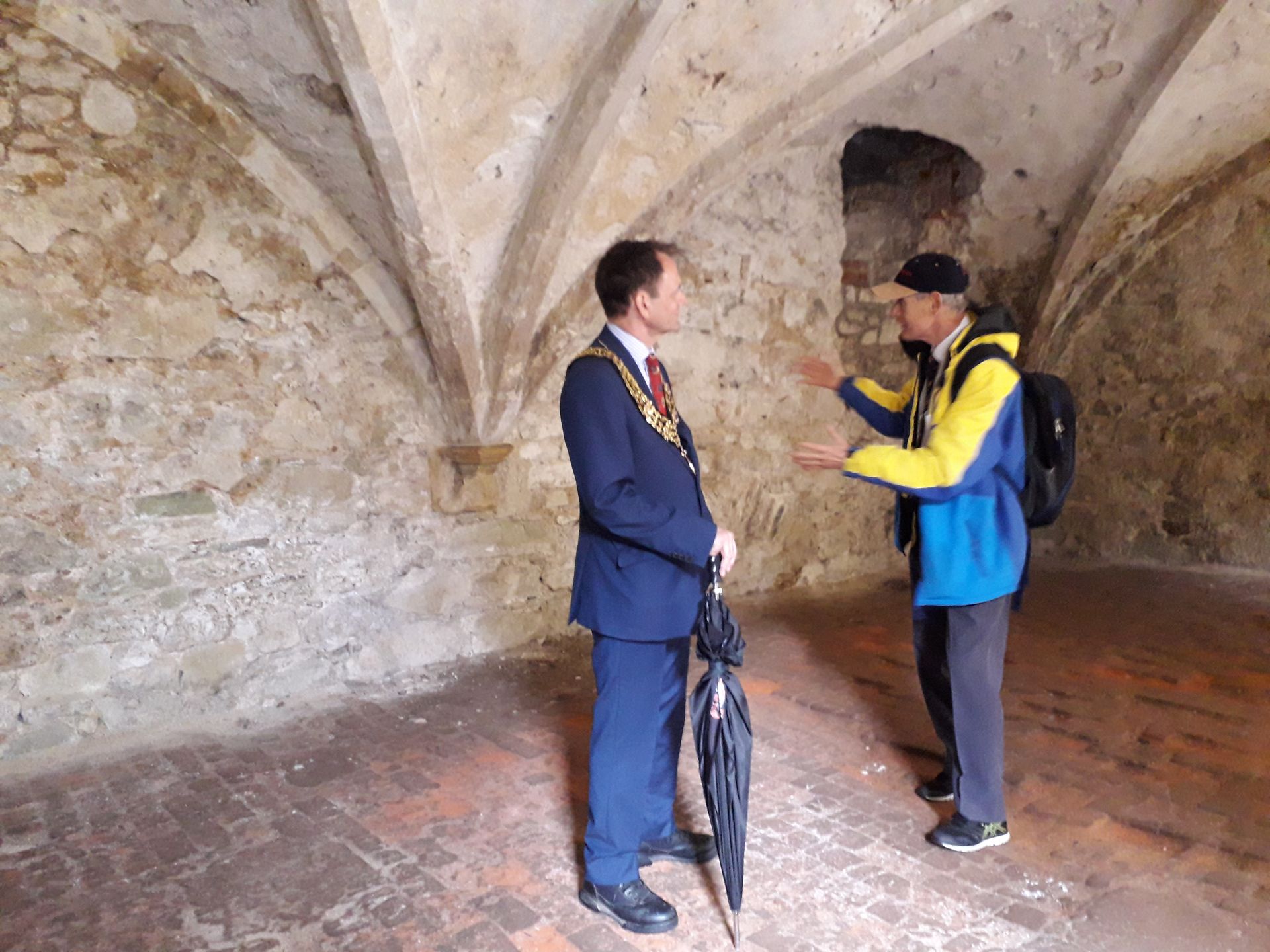Two men are standing in a room talking to each other.