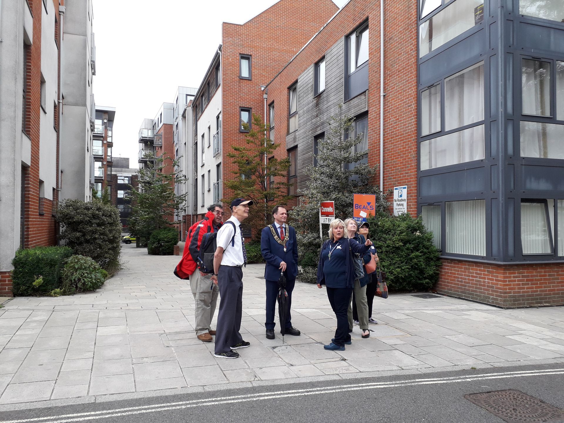 A group of people are standing on a sidewalk in front of a brick building.