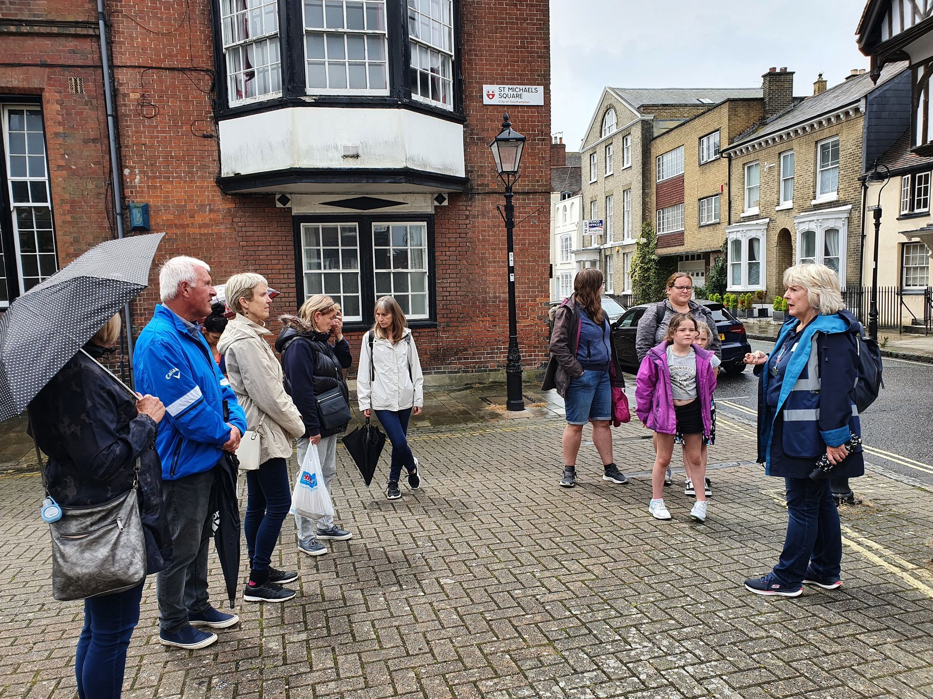 A group of people are standing on a cobblestone street in front of a building.