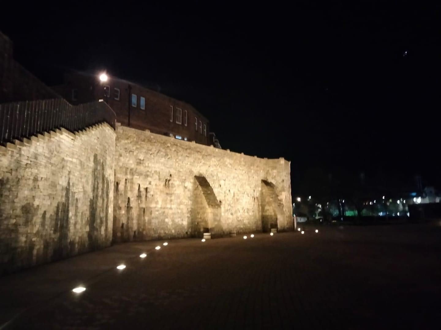 A large stone wall is lit up at night.
