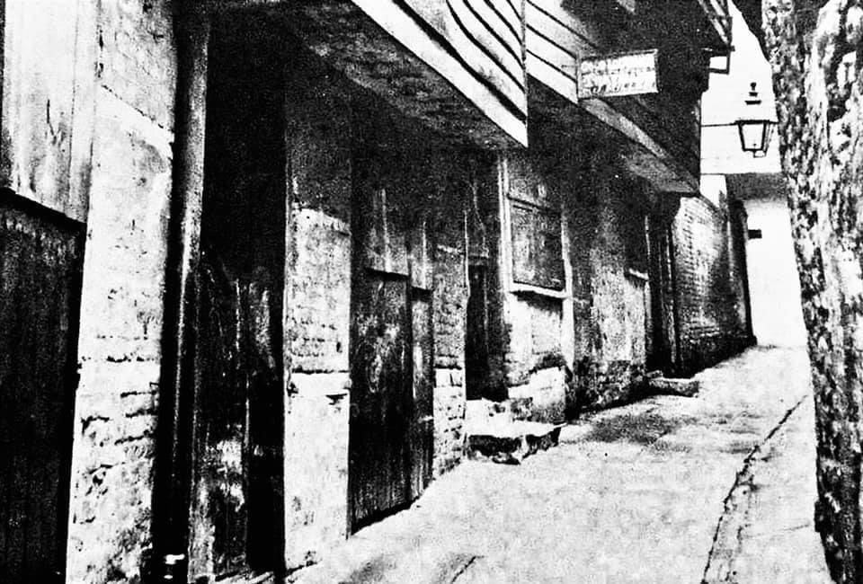 A black and white photo of a narrow alleyway between two buildings.