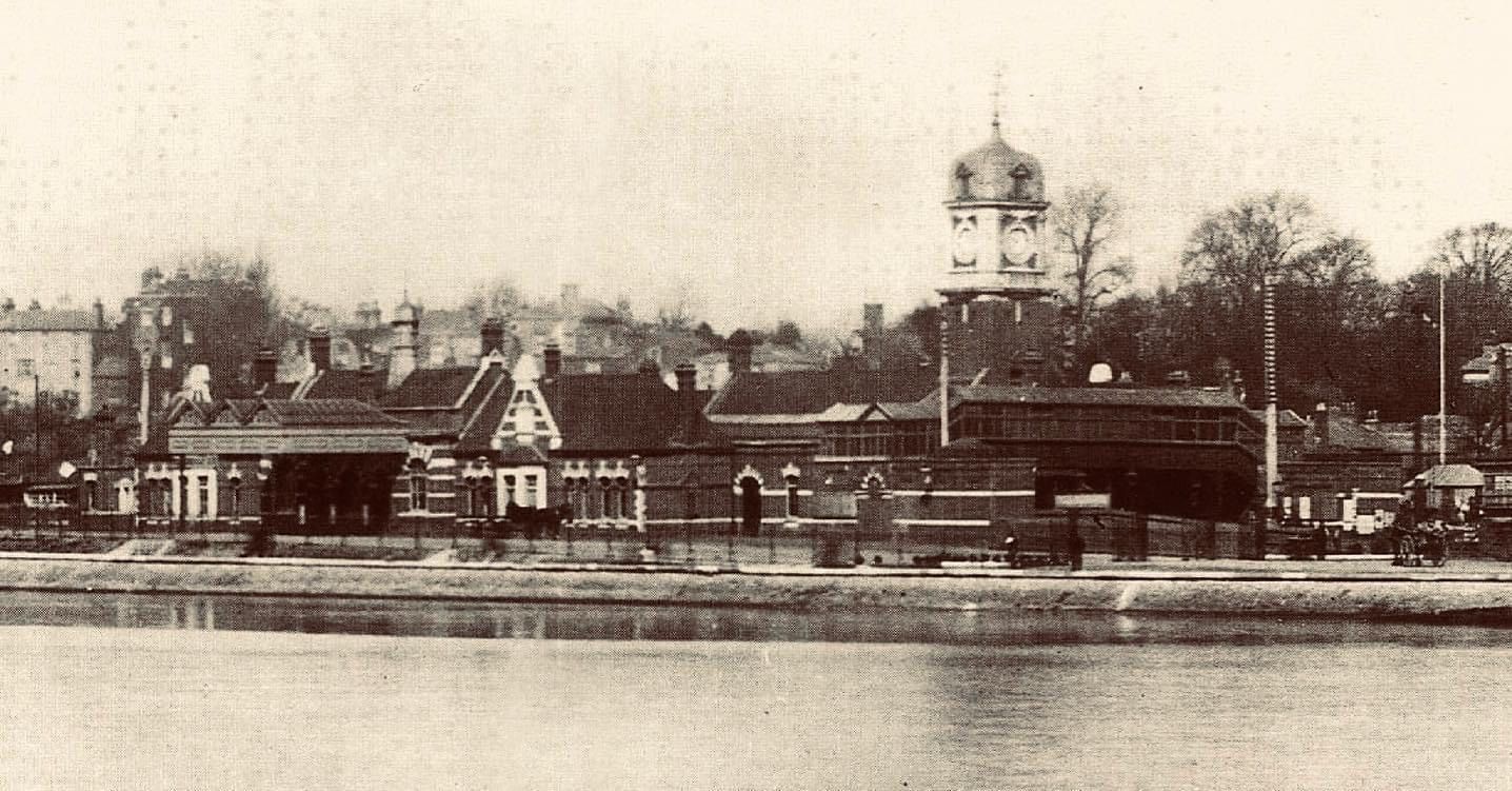 A black and white photo of a train station with a clock tower in the background.