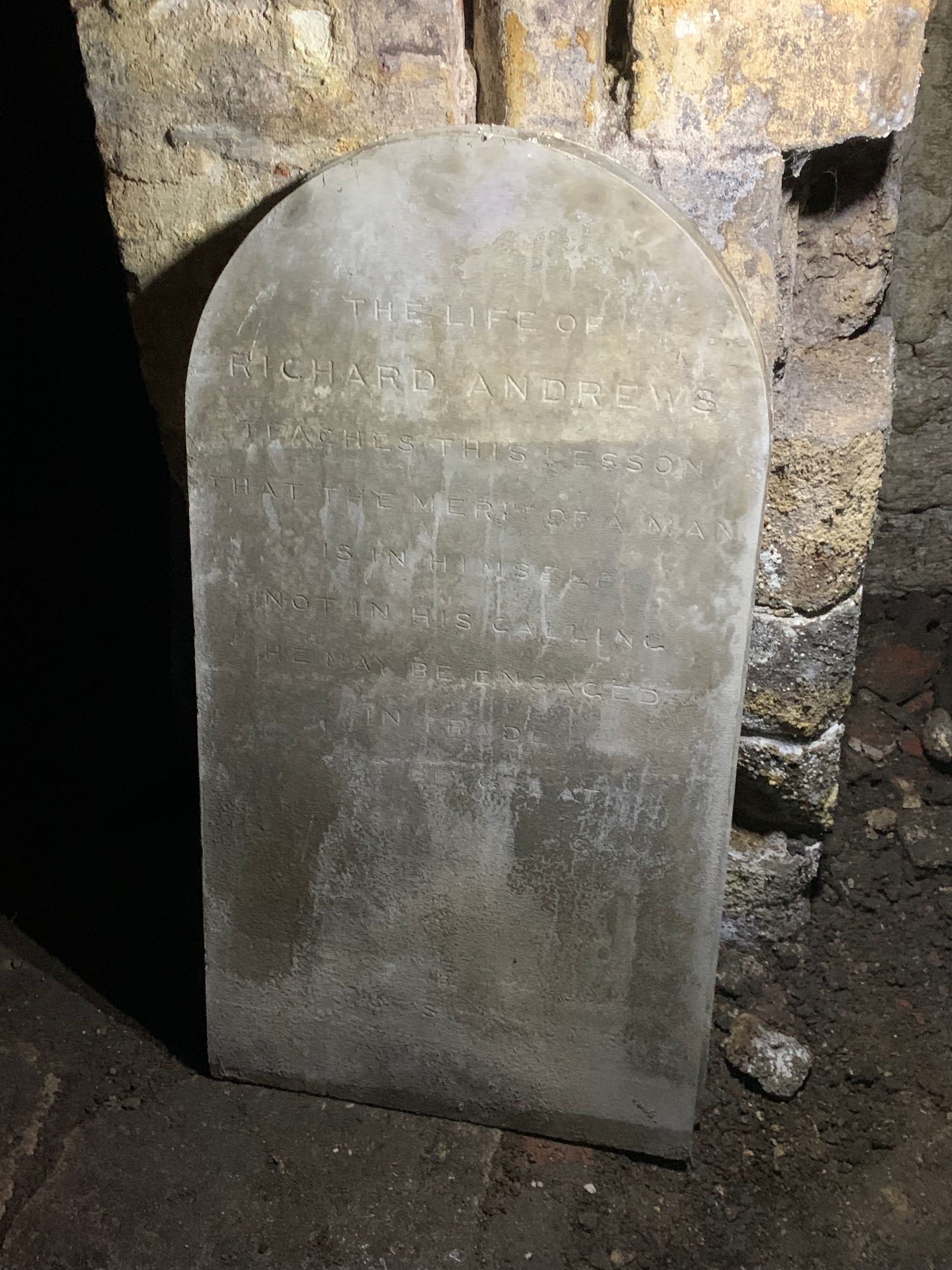 A gravestone is sitting in a dark room next to a stone wall.