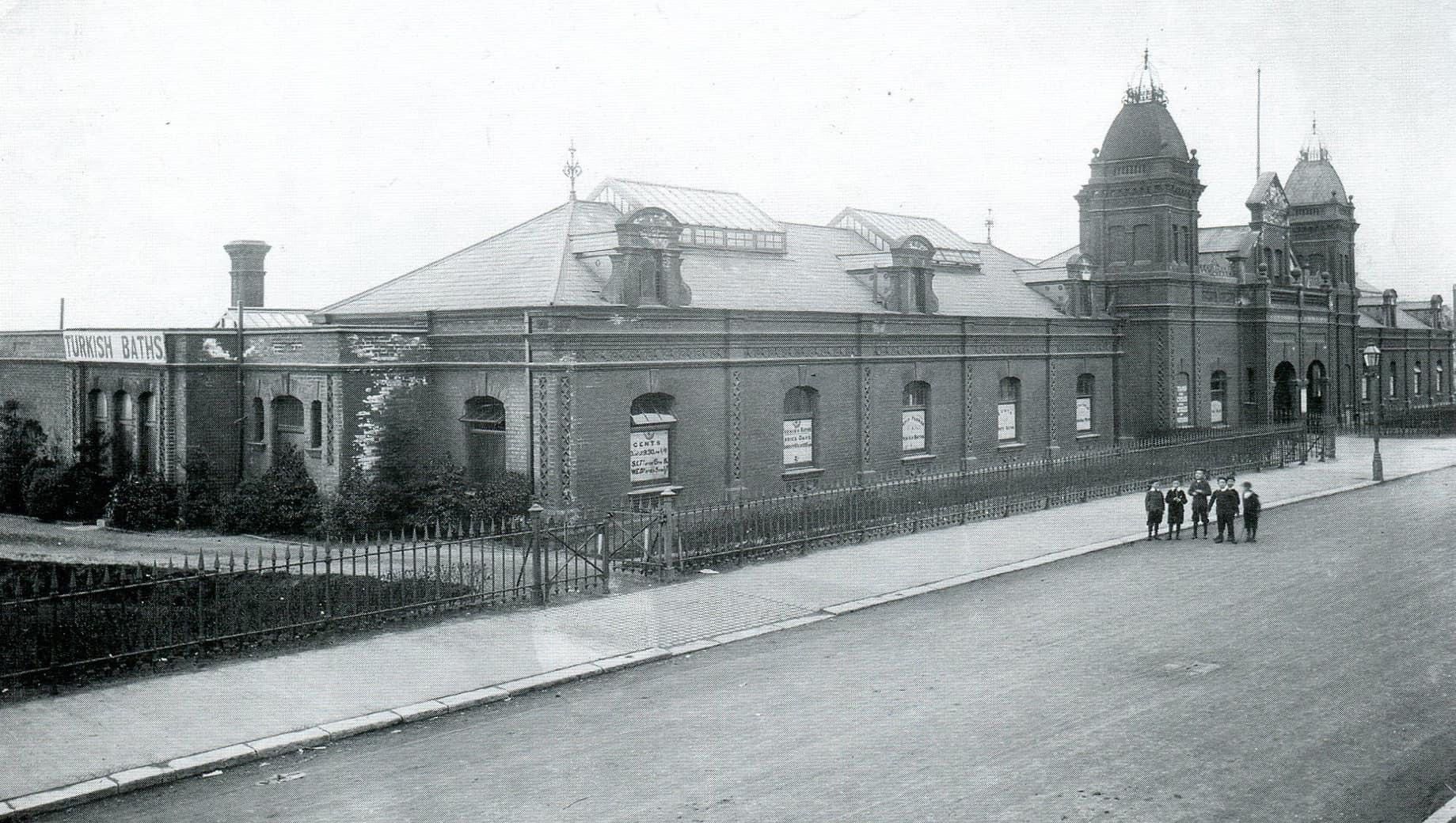 A black and white photo of a large building with people standing in front of it.