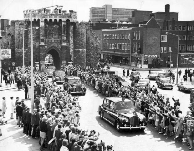 A black and white photo of a row of cars driving down a street