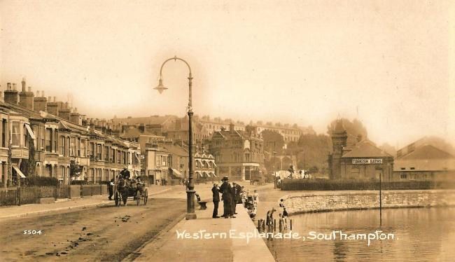 A black and white photo of a city street with a horse drawn carriage.