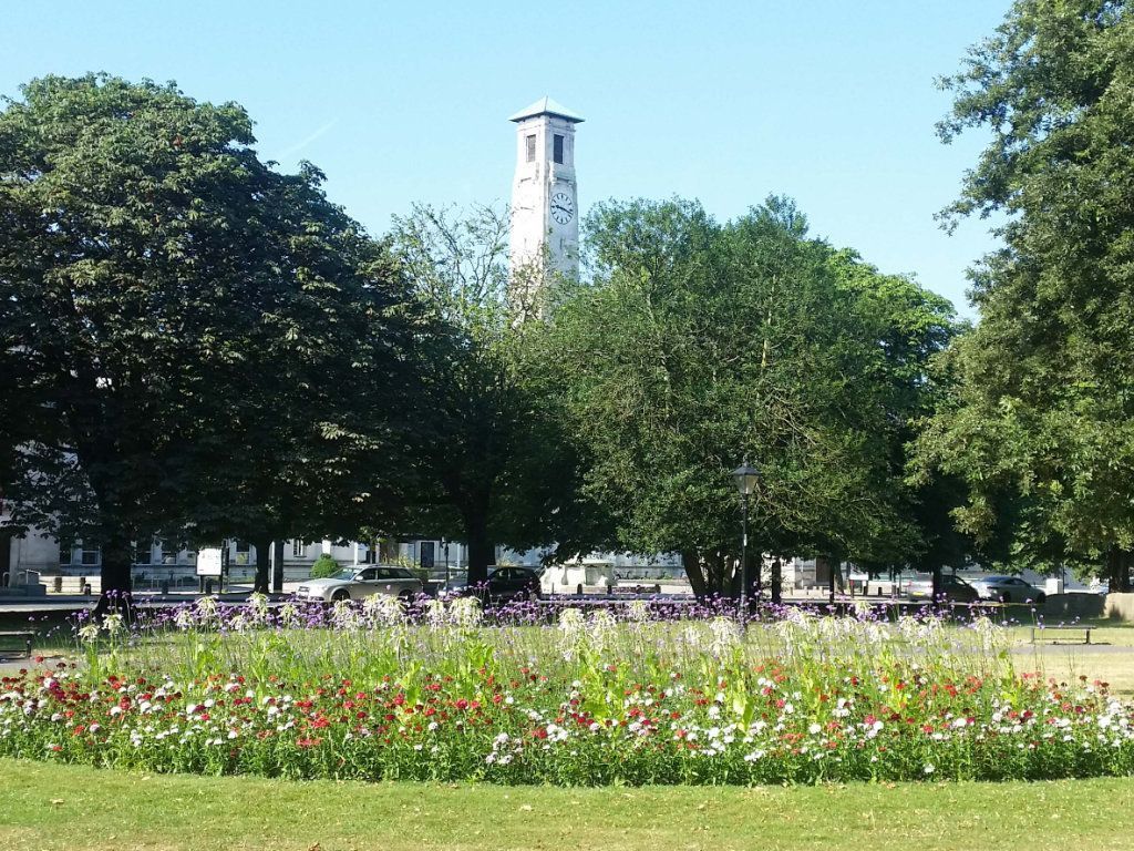 There is a statue in the middle of a park with buildings in the background.