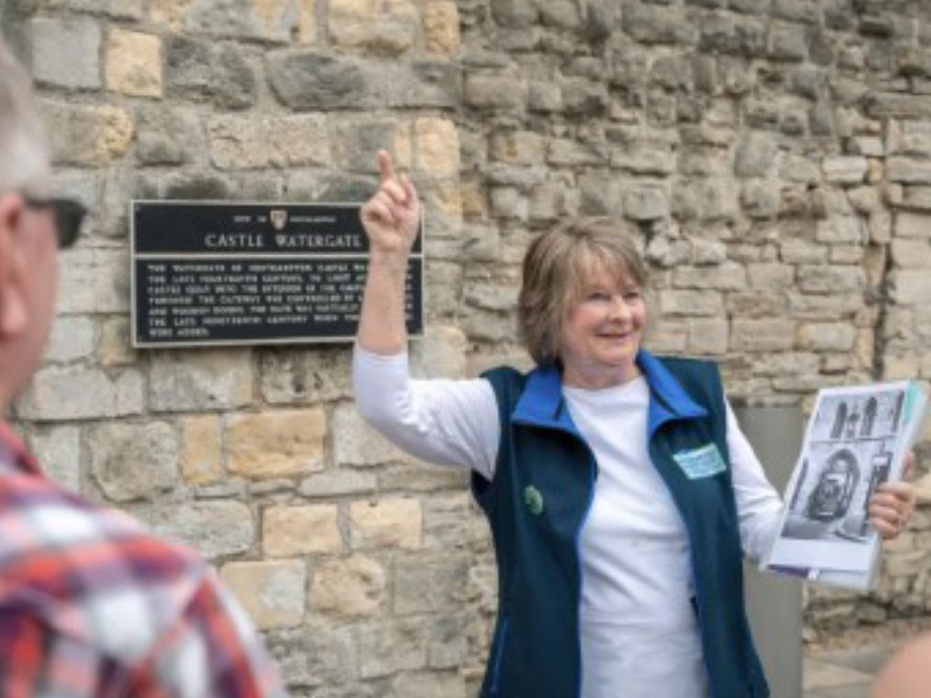 A woman is standing in front of a stone wall holding a piece of paper.