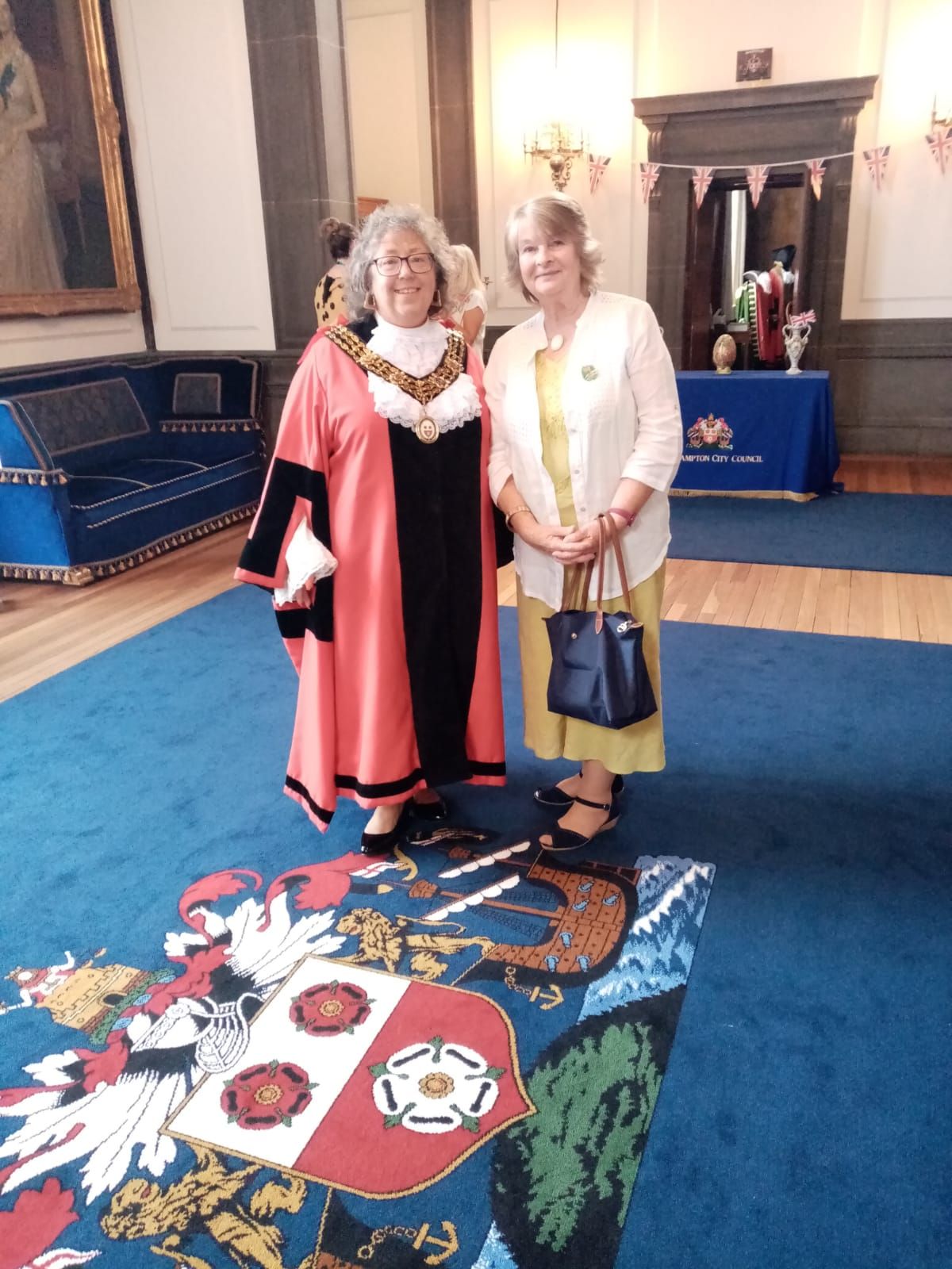 Two women standing next to each other in front of a coat of arms