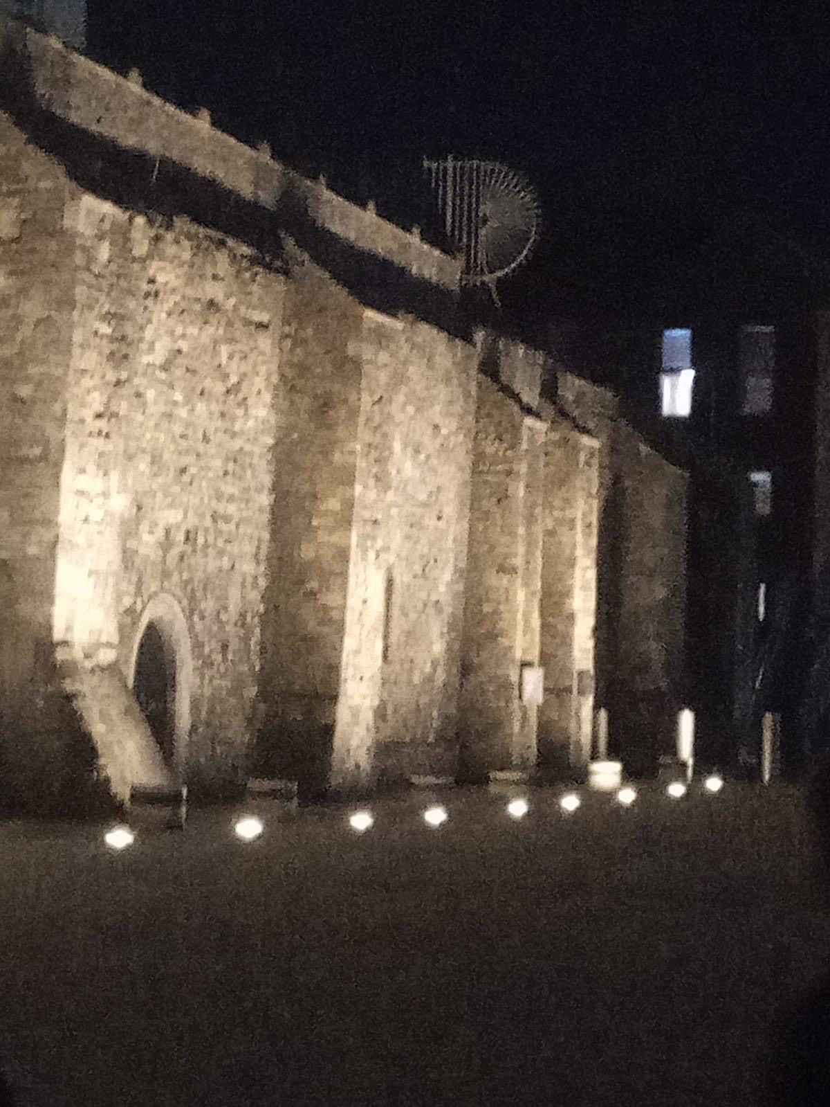 A stone wall is lit up at night with lights on the ground