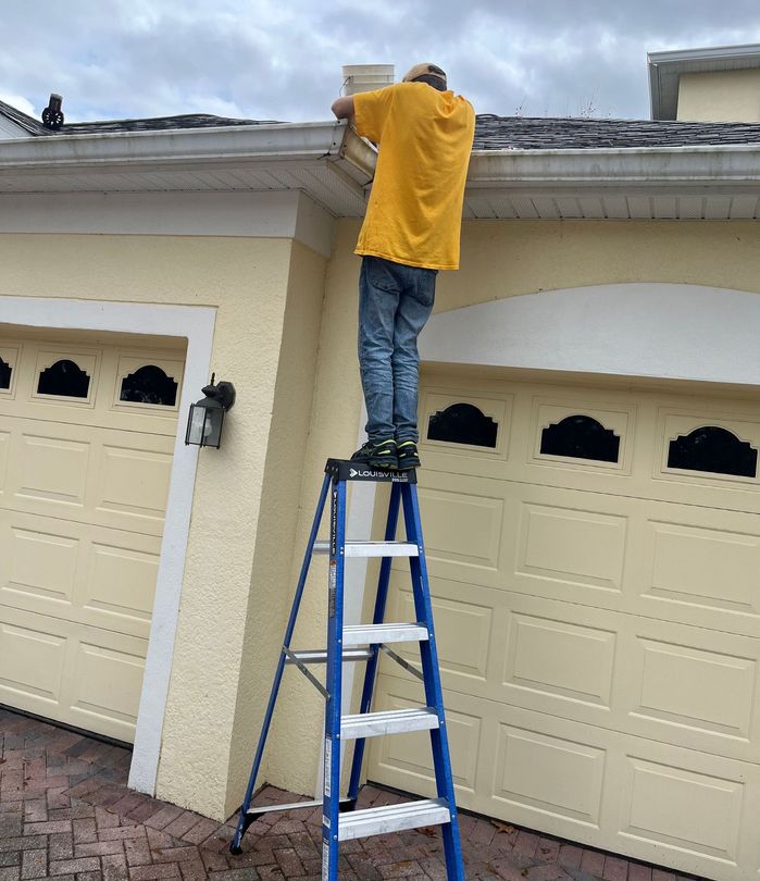 A man is standing on a ladder in front of a yellow garage door.