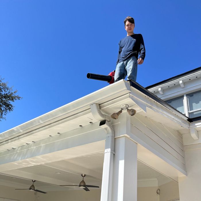 A man is standing on the roof of a house holding a blower