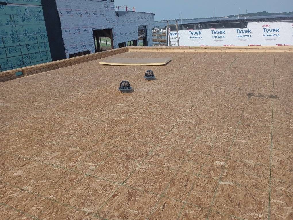 Flat rooftop with gravel surface, two vents, and a raised hatch near the edge of a building.