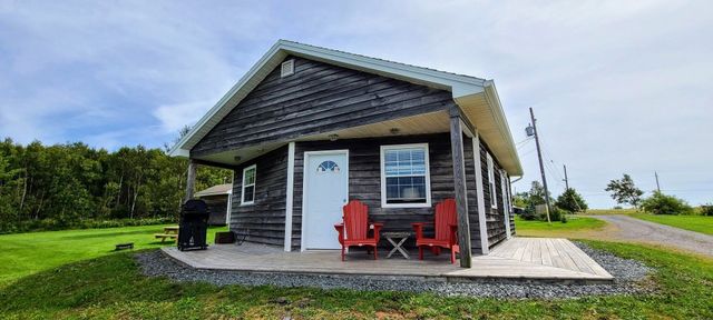 two red chairs on the front porch of a cottage that has wooden plank siding.