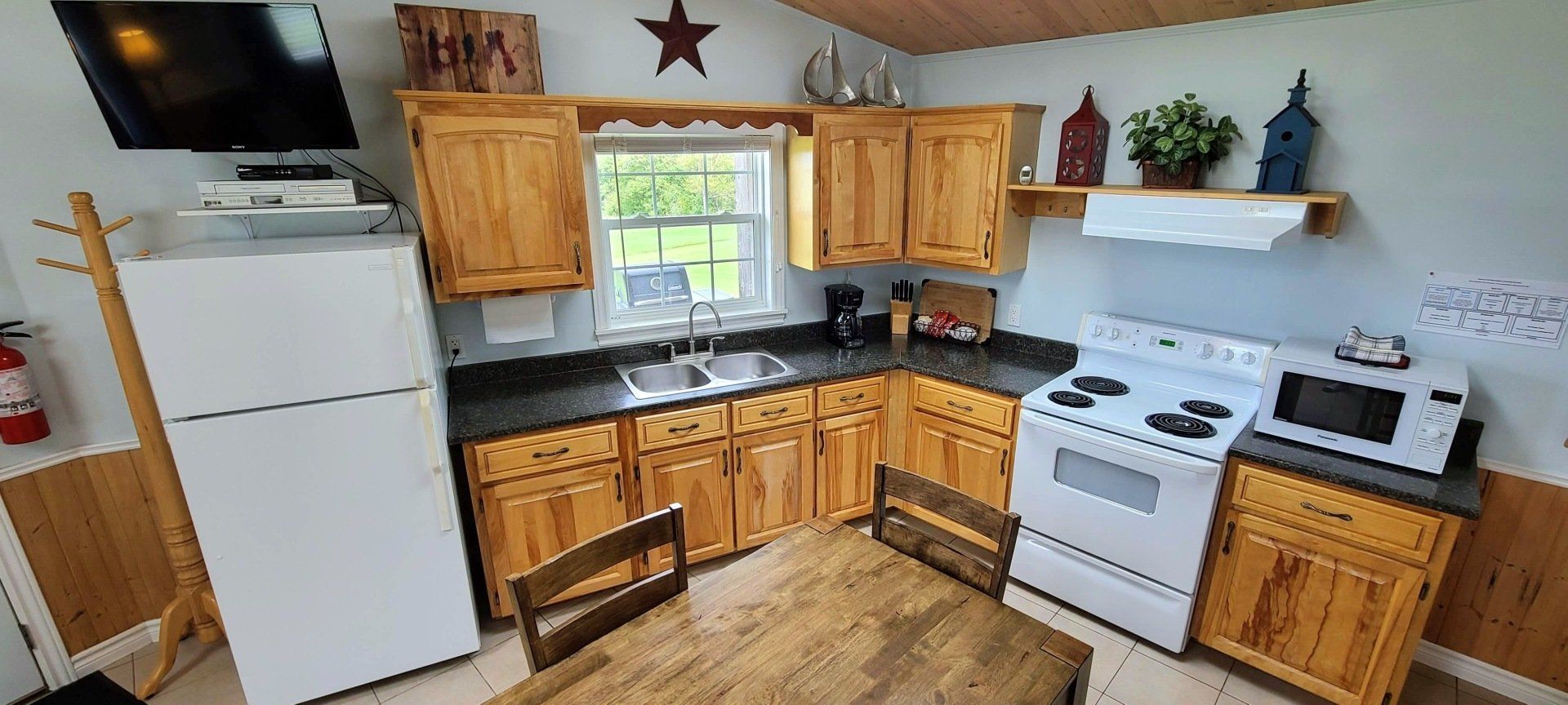 Cottage kitchen area, with fridge, sink under the window, stove, oven, microwave, cupboards, and a kitchen table.