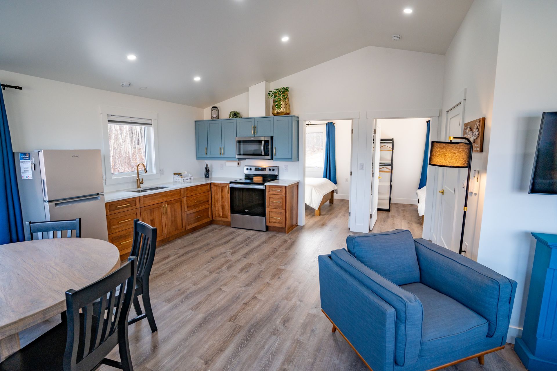 Cottage kitchen area, with fridge, sink under the window, stove, oven, microwave, cupboards, and a kitchen table.