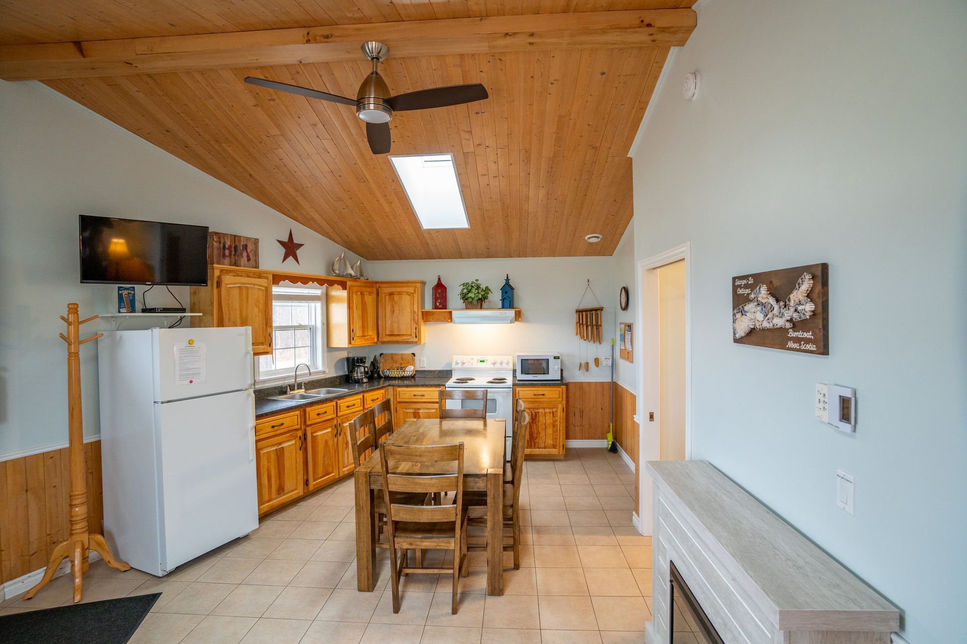 Cottage kitchen area, with fridge, sink under the window, stove, oven, microwave, cupboards, and a kitchen table.