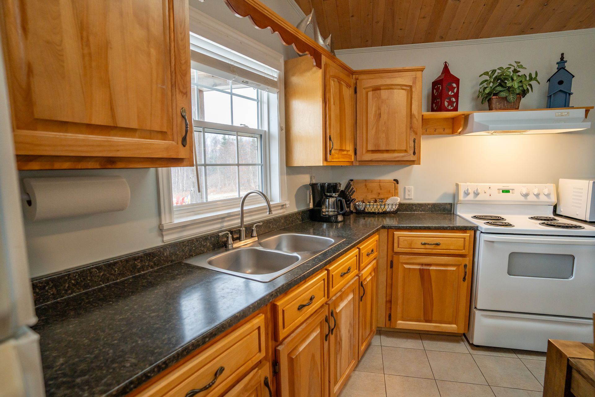 Cottage kitchen area, with fridge, sink under the window, stove, oven, microwave, cupboards, and a kitchen table.