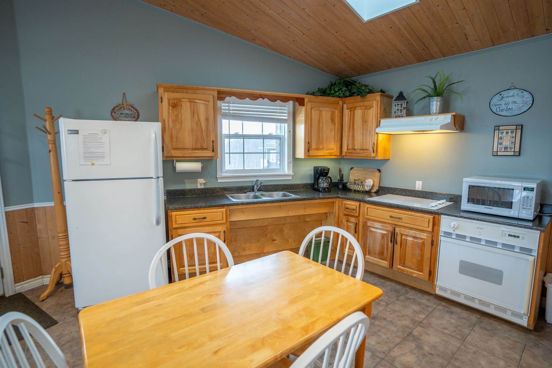 Cottage kitchen area, with fridge, sink under the window, stove, oven, microwave, cupboards, and a kitchen table.