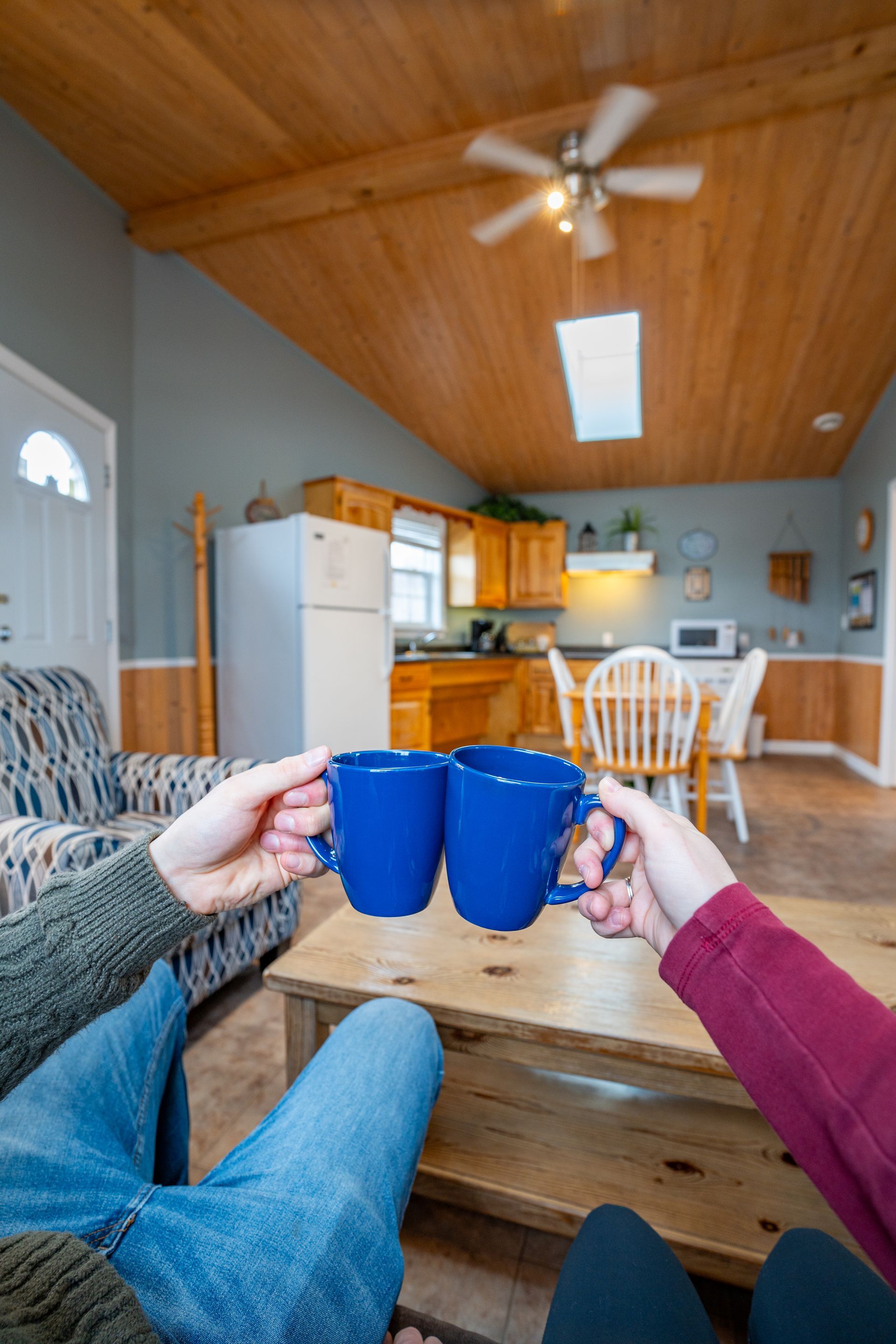 two hands with blue coffee mugs. kitchen area, with fridge, sink, stove, oven, microwave, cupboards, and a kitchen table.