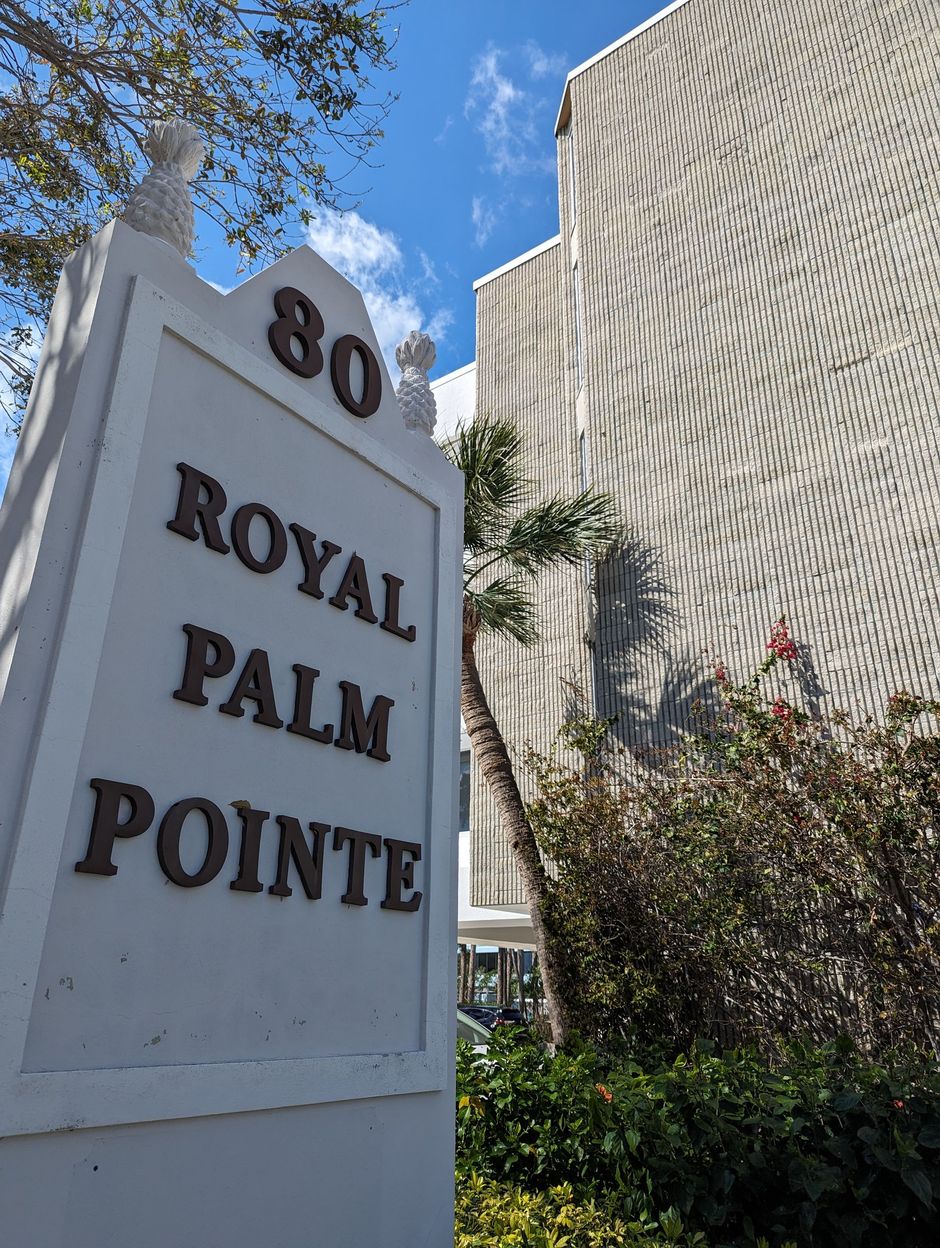 Aerial view of a beach with golden sand, turquoise water, and a highway with green golf courses and houses.