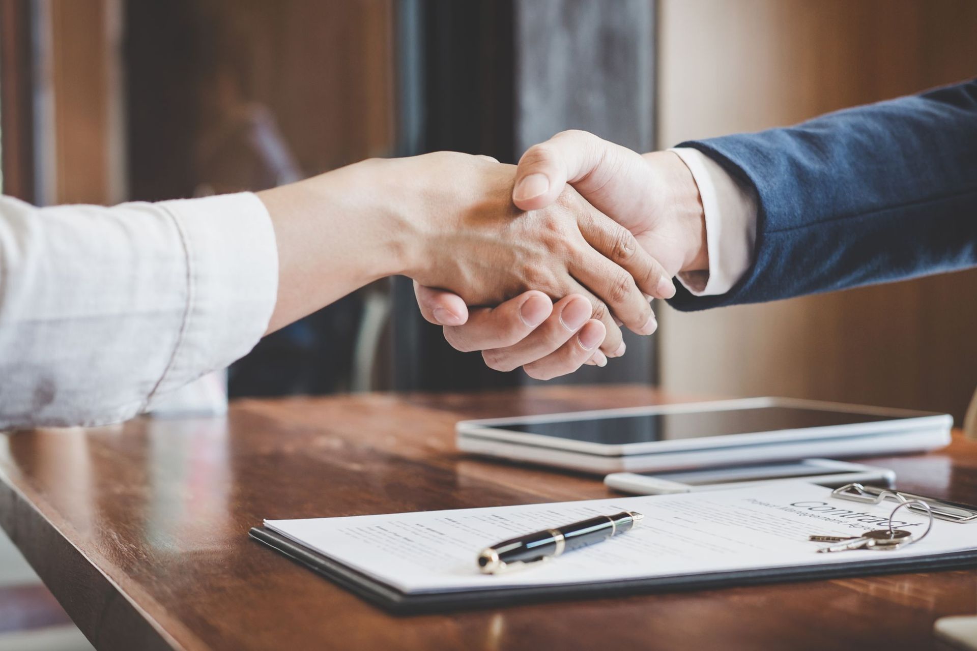 Two people shaking hands over a table with a document and pen.