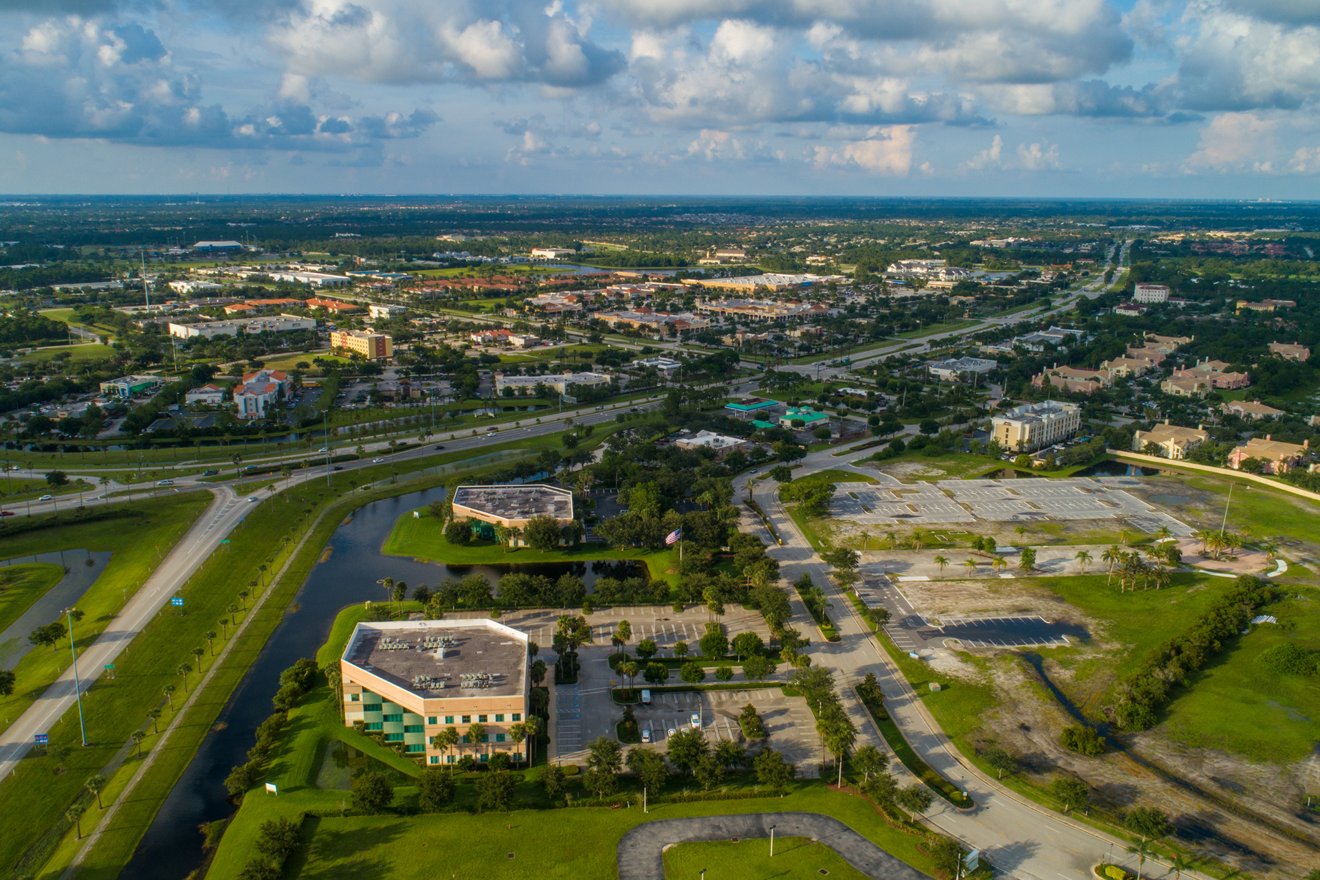 Aerial view of a suburban cityscape with buildings, roads, and green spaces under a cloudy sky.