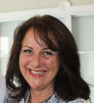 Woman with dark hair smiles; light blue patterned top.