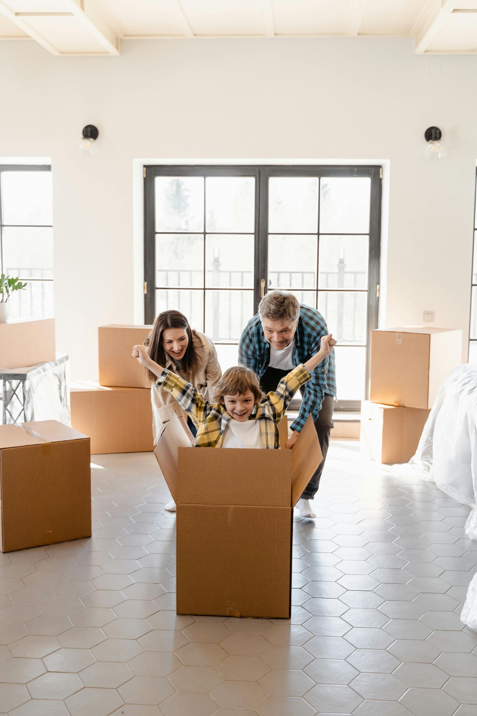 Family moving into a new home, a child inside a cardboard box being pushed by the parents.