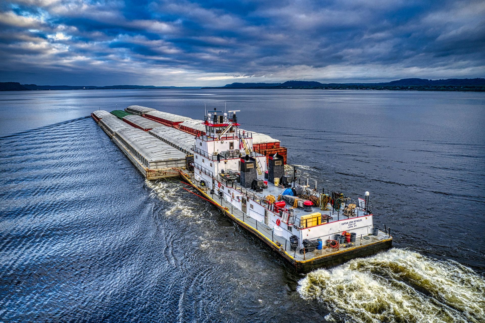 Barge sailing on water under a cloudy sky.