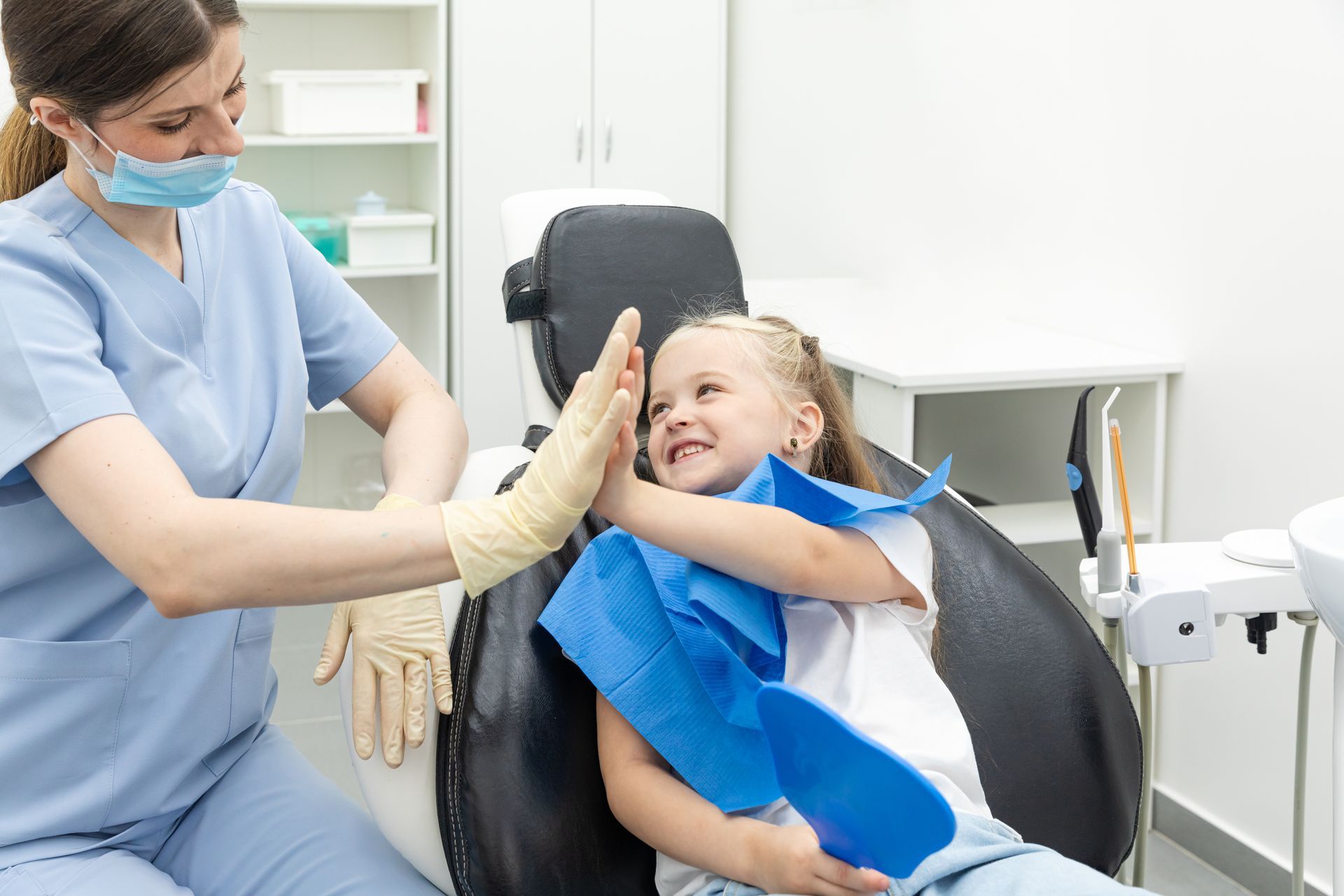 Little patient girl sitting in a chair gives a high five to a pediatric dentist.