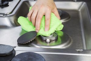 A person is cleaning a stove top with a green cloth.