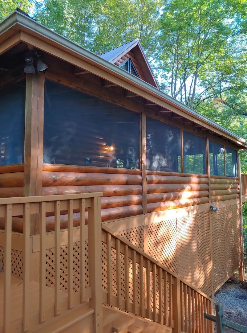 Log cabin with screened porch and wooden stairs, nestled in a wooded area.