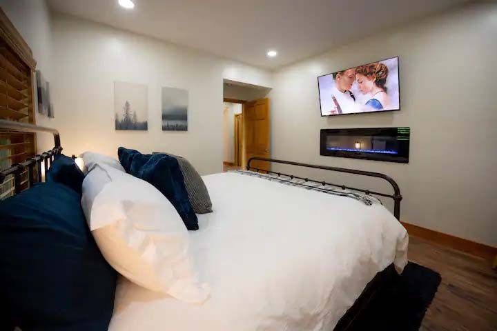 Bedroom with bed, TV, fireplace, and two landscape paintings on the wall.