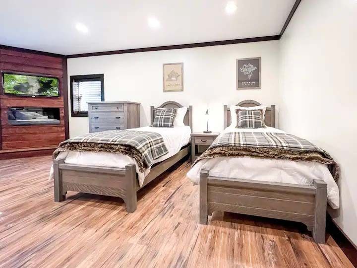 Two twin beds in a rustic bedroom with a dresser, TV, and wood floors.