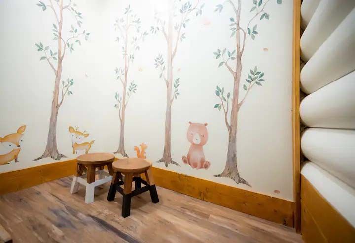 A cozy corner with a forest mural, wooden stools, and log-style paneling.