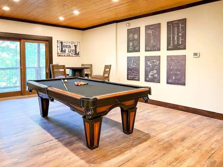 Pool table in a room with a seating area, wood floor, and framed prints on the wall.