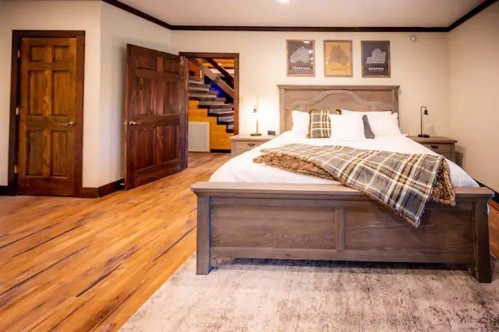 Bedroom with a wooden bed, flooring, and doors. Stairs lead up, and art hangs above.