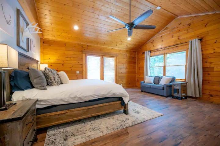 Bedroom with wooden walls, vaulted ceiling, and king-size bed, featuring a couch and window.