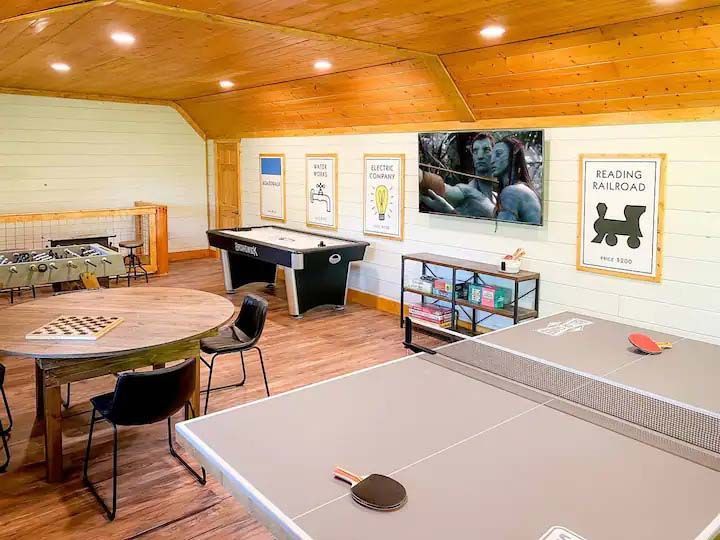 Recreation room: ping pong, pool, TV, games, round table with chairs, wood and light walls.