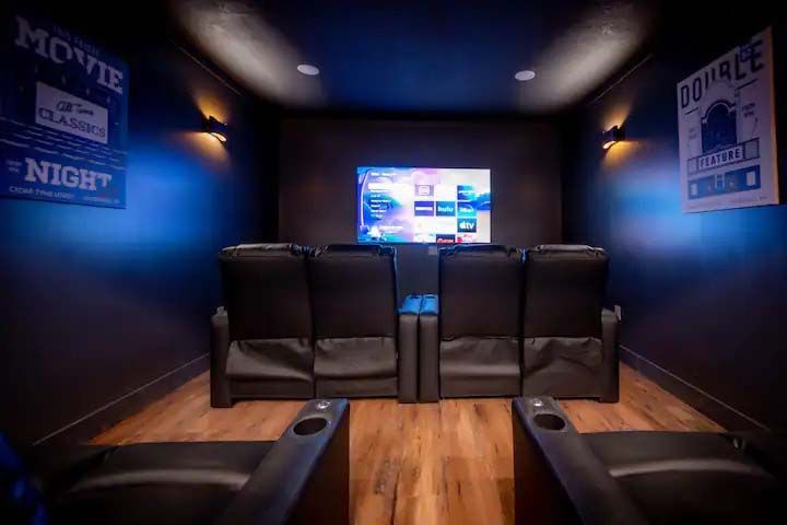 Home theater with black leather recliners, screen, movie posters, and blue ambient lighting.
