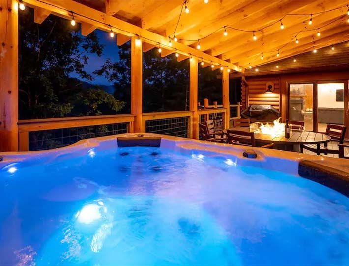 A hot tub on a covered wooden deck lit with string lights.