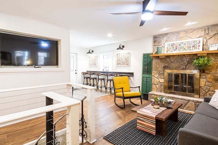 Living room with stone fireplace, TV, bar seating, and yellow rocking chair.