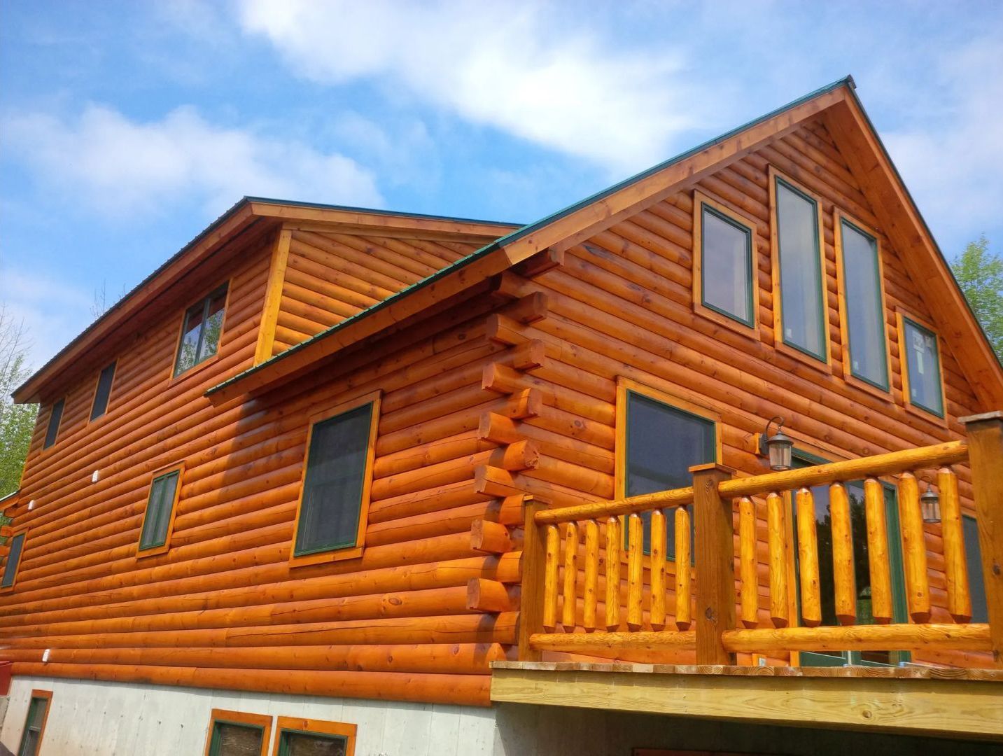 Log cabin with wood exterior, deck, and windows against a blue sky.