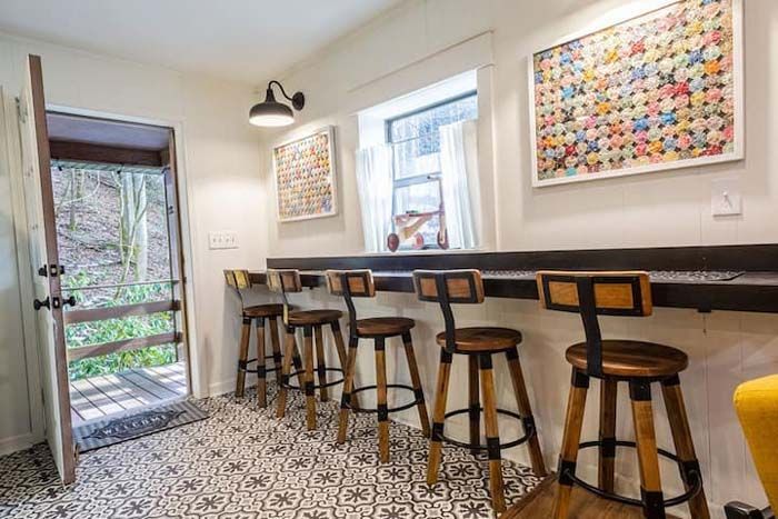 A room with a bar counter and stools, artwork, and a door to an outdoor deck.