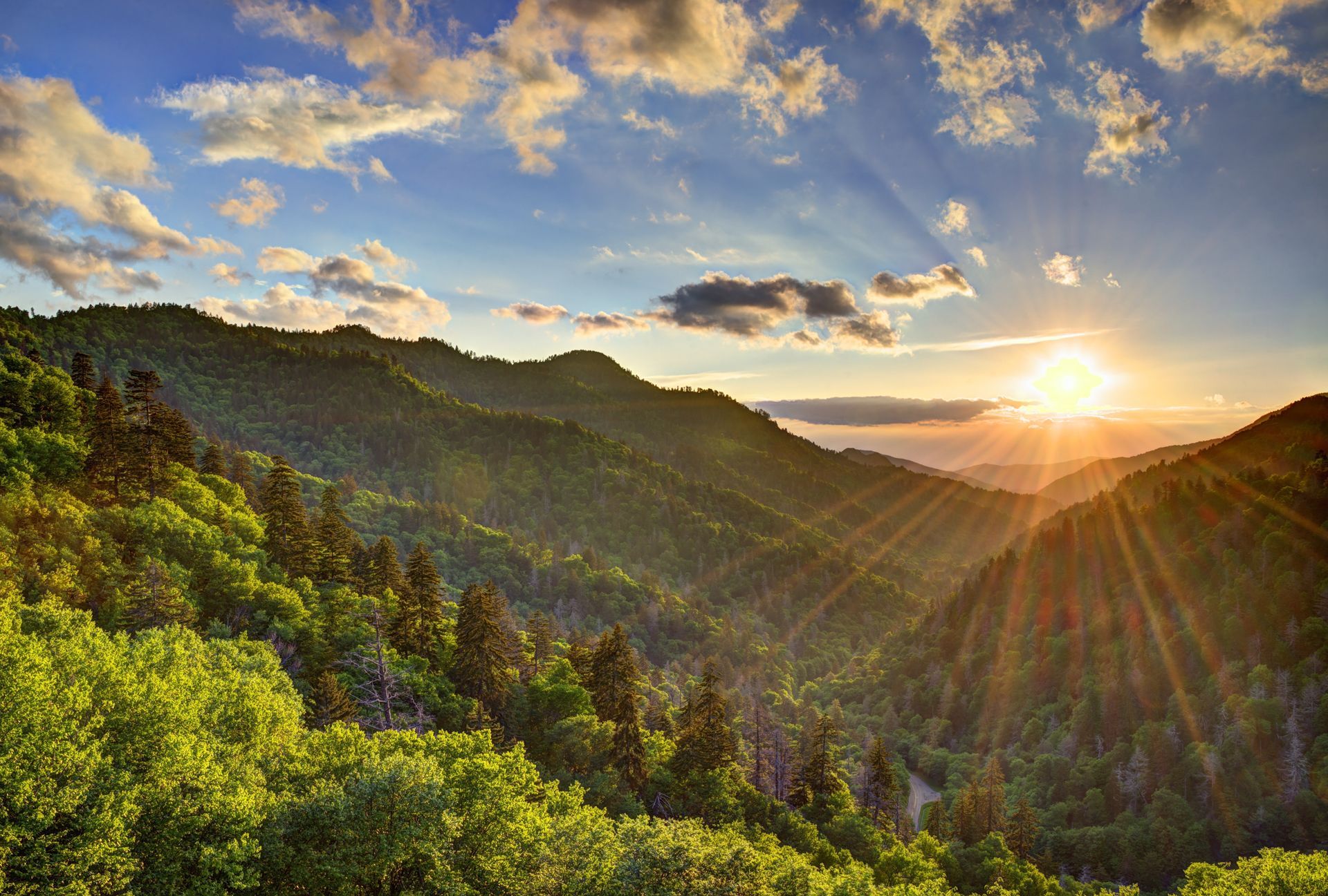 Sunrise over lush, green mountains; sunbeams burst through clouds.