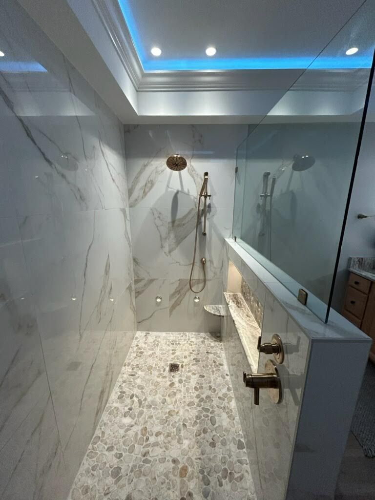 Luxurious marble-tiled shower with pebble floor, gold fixtures, and a glass enclosure. The room has ambient blue lighting.