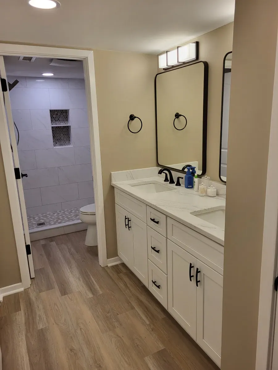 Modern bathroom with white vanity, black fixtures, large mirrors, and a walk-in shower with gray tile.